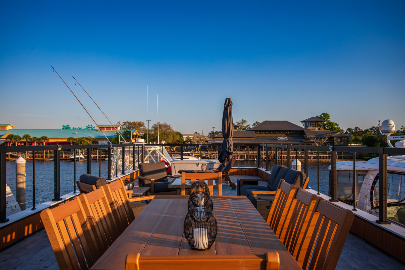 Eight-seat rooftop dining table looking out across the marina toward the Barefoot Landing waterfront shops and restaurants, with lounge seating and the Intracoastal Waterway on both sides.