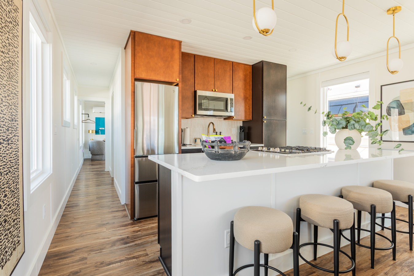 Fully equipped kitchen with quartz island countertop, gas stove, gold pendant lighting, bar seating for four, and a glimpse of the king bedroom through the hallway.