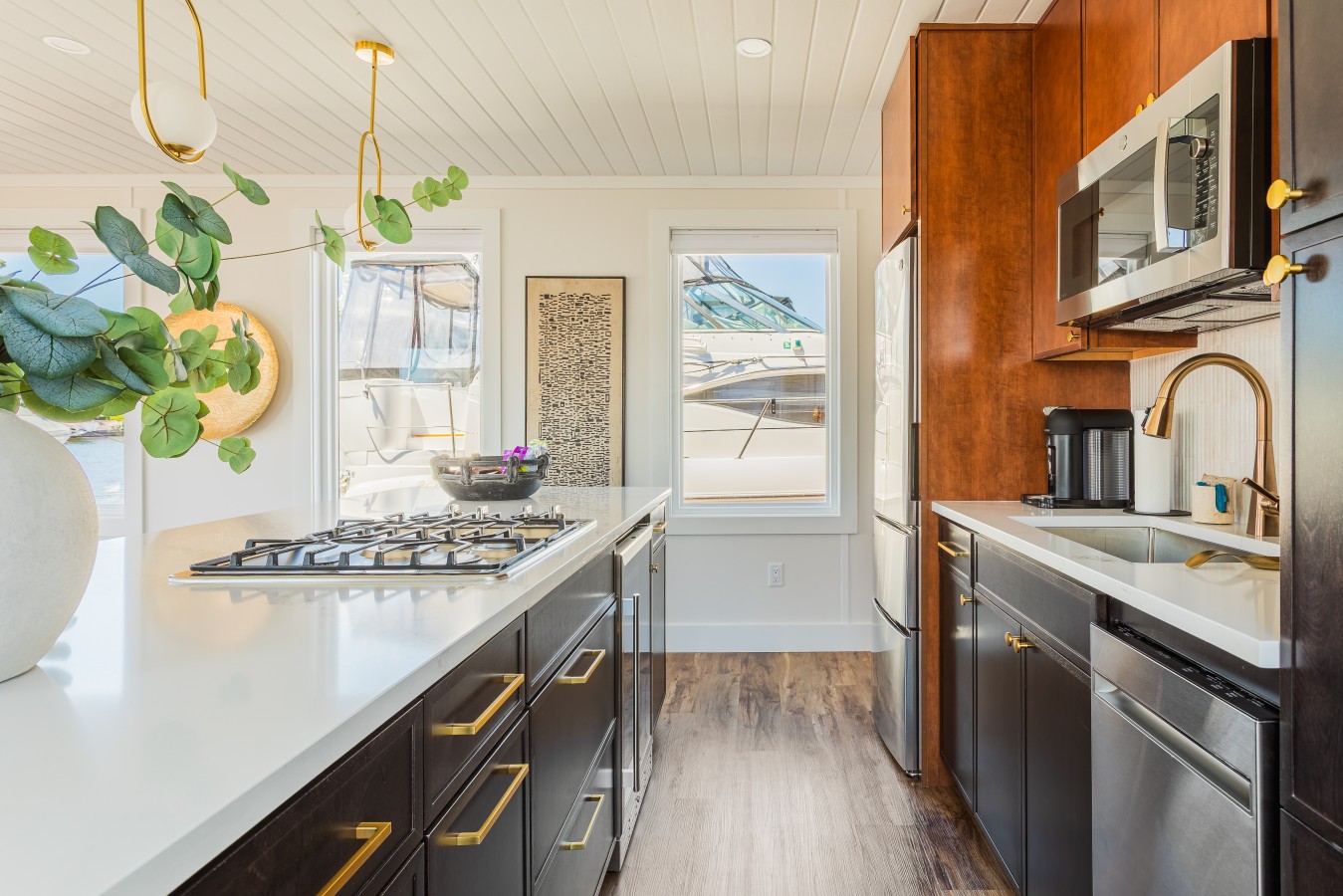 Kitchen detail showing the gas stove, stainless steel appliances, gold hardware, coffee station, and marina views through the windows with boats docked along the Intracoastal.