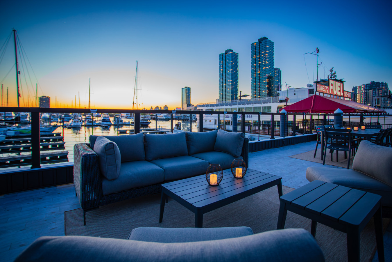 The rooftop lounge sets the mood at dusk, with deep seating, candlelit lanterns, and a full marina view stretching out in every direction.