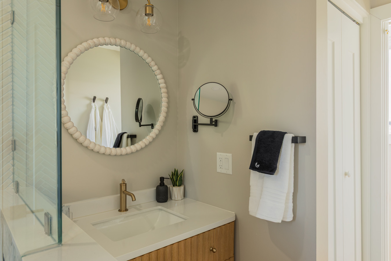 The vanity is finished with a brass faucet, textured round mirror, and warm globe lighting — details that feel more boutique hotel than short-term rental.