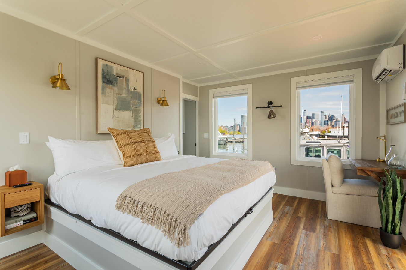 The king bedroom wakes up to direct views of the Manhattan skyline, with gold sconce lighting, a workspace nook, and a private door to the water.