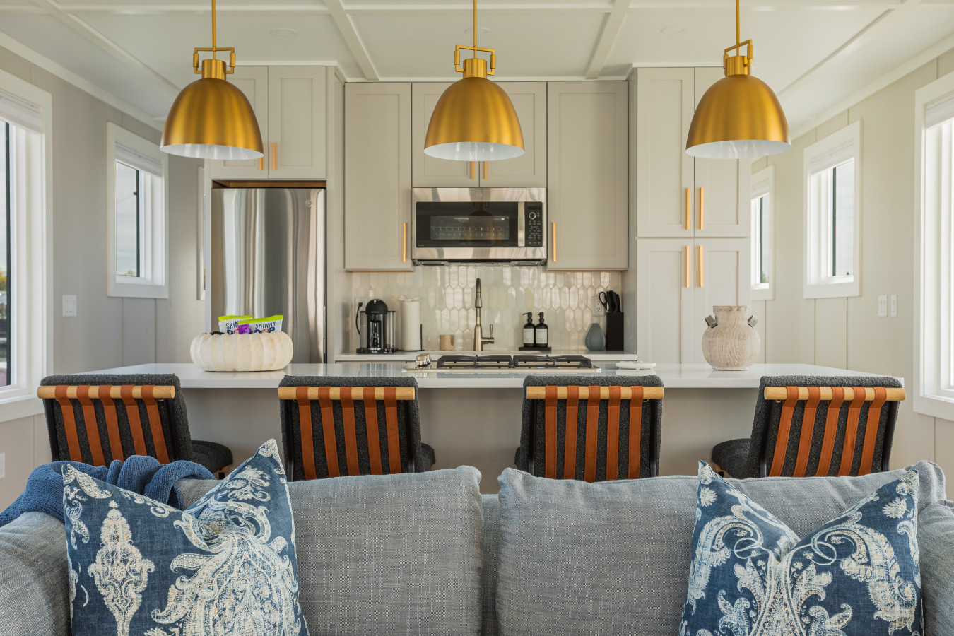 Three brass pendants anchor the kitchen, with a ceramic tile backsplash, Nespresso station, and bar seating that keeps the conversation flowing between the living area and the cook.