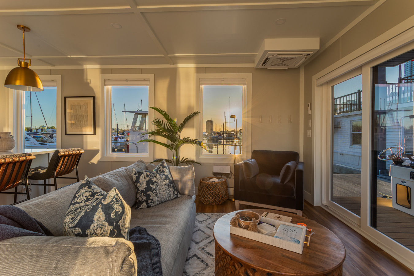 The living area at golden hour, with warm light across the water, a sliding door open to the private deck, and the whole suite glowing from end to end.
