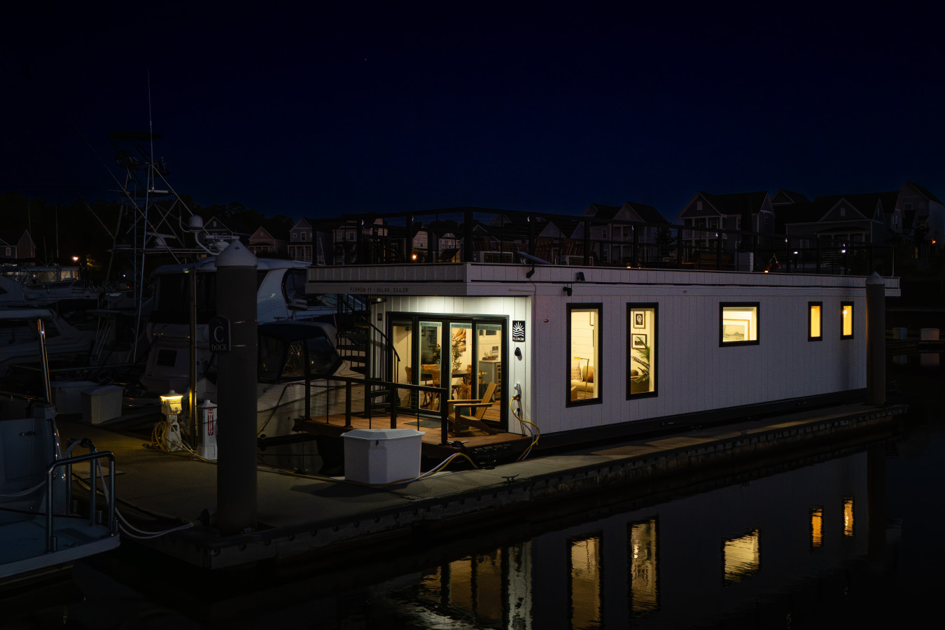 Selah Sailor glowing from within at night, docked at Barefoot Marina with its own reflection mirrored in the still water below.