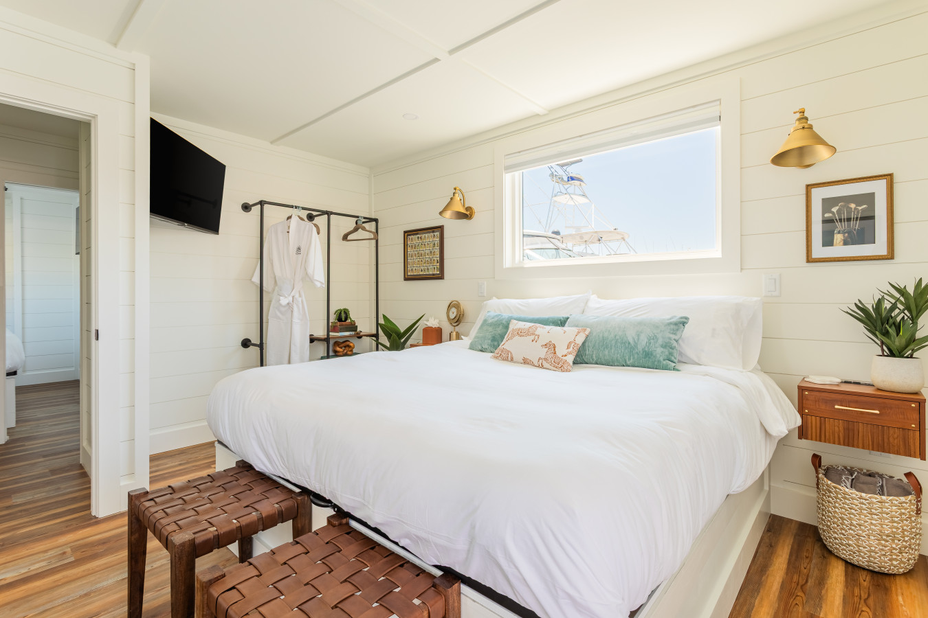 A private king master suite with shiplap walls, brass sconce lighting, a marina window view, complimentary robes, and a dedicated en-suite bathroom just through the door.