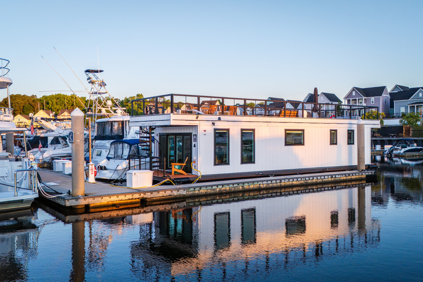 Selah Sailor in full morning light at Barefoot Landing Marina, with the rooftop deck, open waterway, and the property's reflection stretching across the still water below.