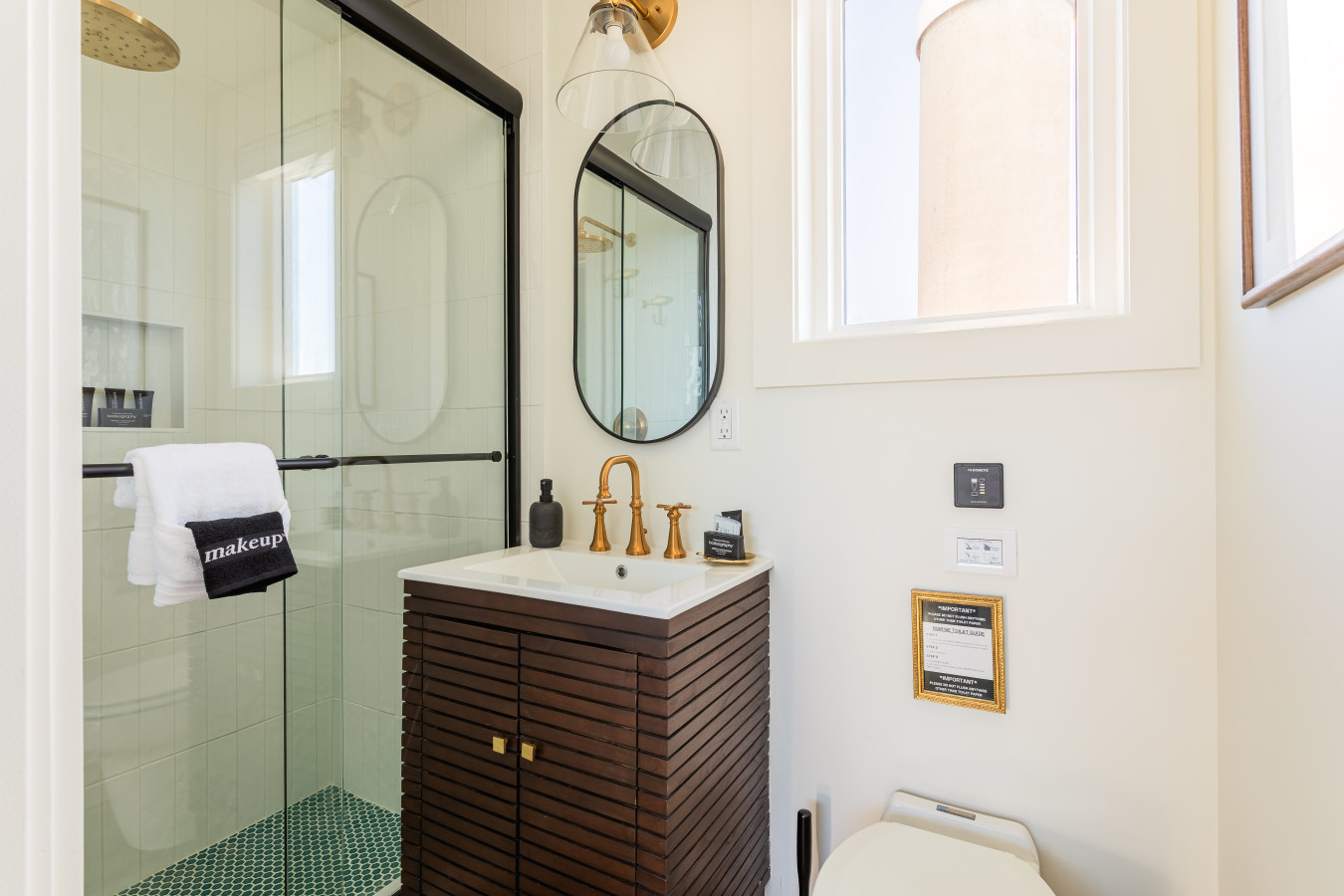 Master bathroom two with a walnut vanity, brass fixtures, oval mirror, glass pendant sconce, and a walk-in shower with green penny tile flooring.