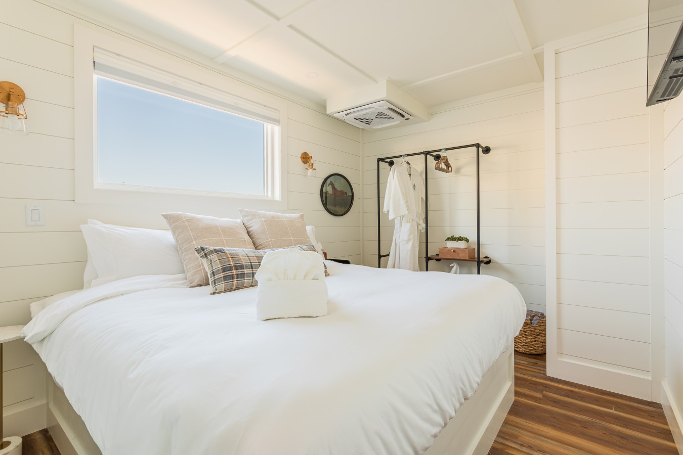 The second private king master suite, individually styled with warm plaid linens, shiplap walls, brass sconce lighting, a FLOHOM robe on the open wardrobe rack, and its own en-suite bathroom just through the door.