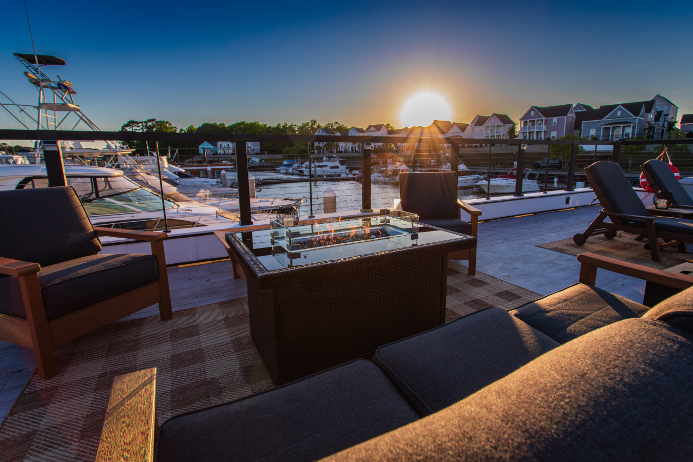 The rooftop fire pit and lounge seating at sunrise, with the sun cresting the Barefoot Landing waterfront homes and the marina stretching out on both sides.