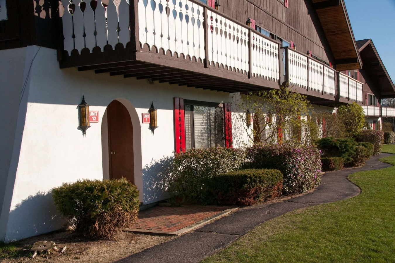 Charming alpine-style condo with rustic balconies, red shutters, and lush landscaping, offering a cozy retreat near outdoor adventures.