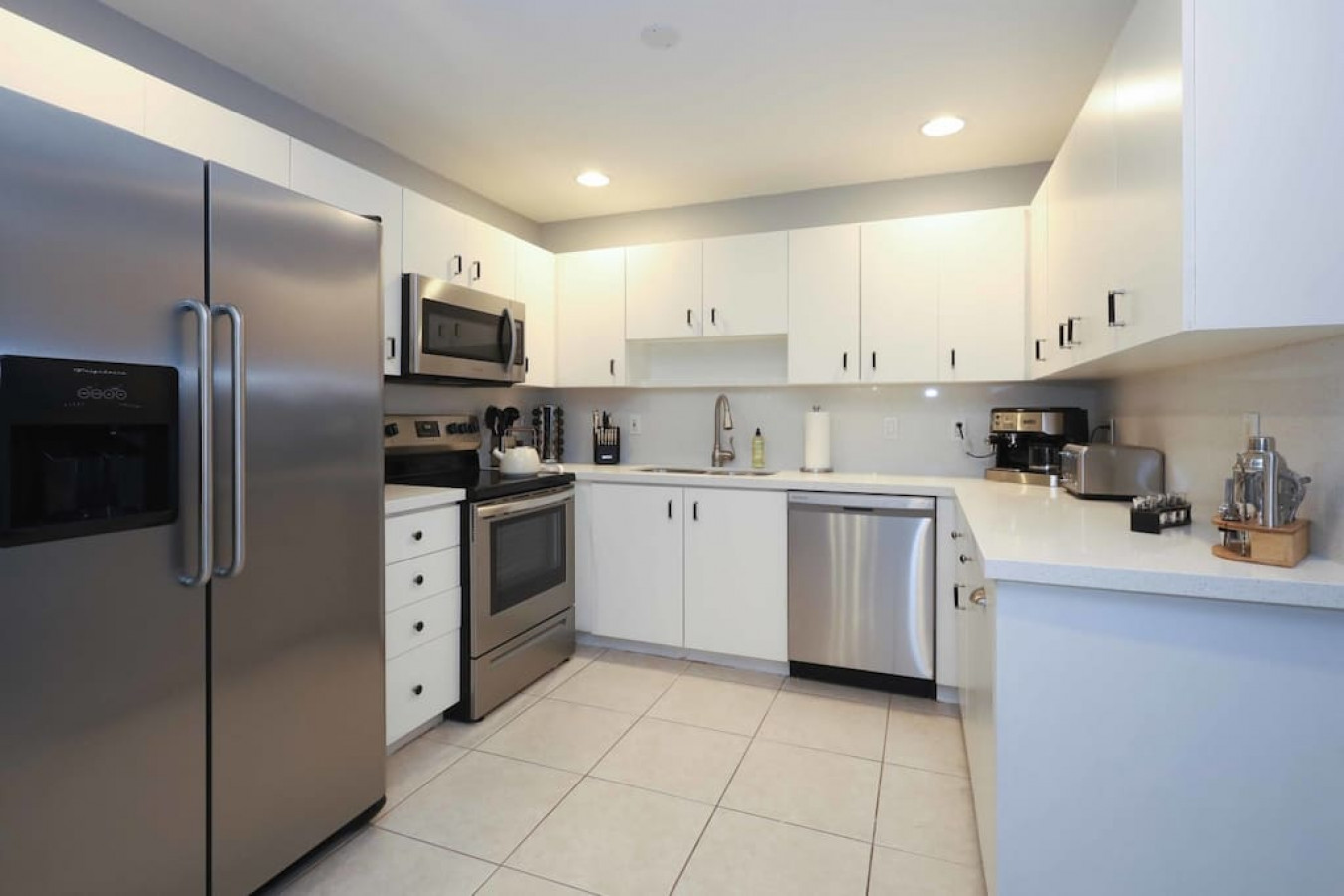 The fully-stocked, designer kitchen has French white cabinets, ample storage space, quartz countertops, high gloss tile backsplash, and stainless steel appliances