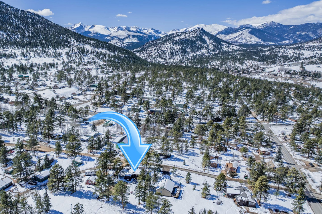 Aerial image of snow-covered mountains, evergreen trees, roads, and buildings with a blue arrow pointing toward a building.